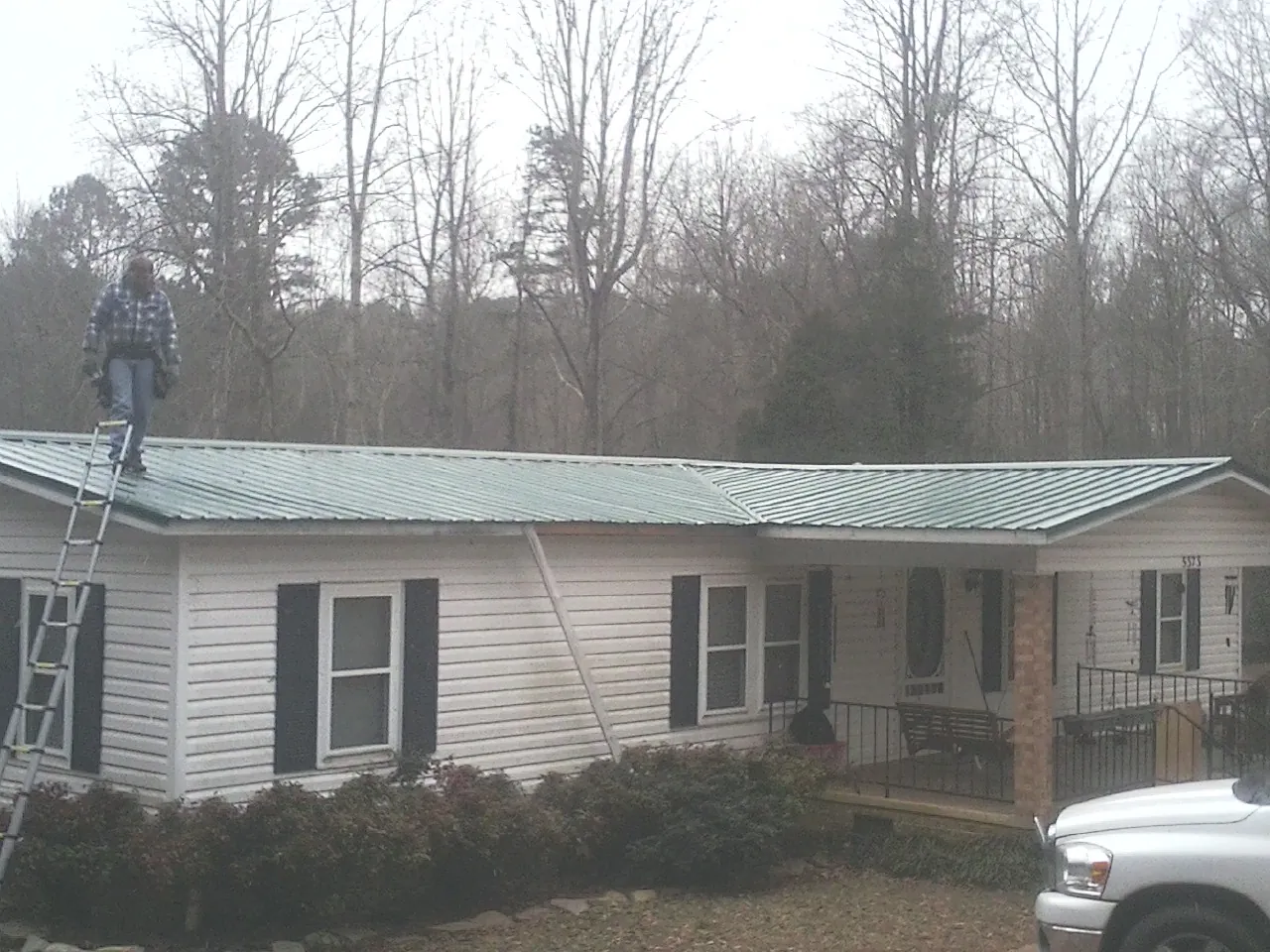 Worker on a ladder beside a new green metal roof on a ranch home in Pownal