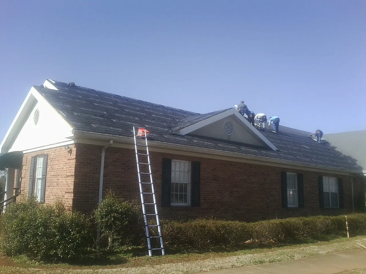 Crew tearing shingles off a brick ranch roof with a ladder set — Metal Roof Repair work by our crew in Pownal